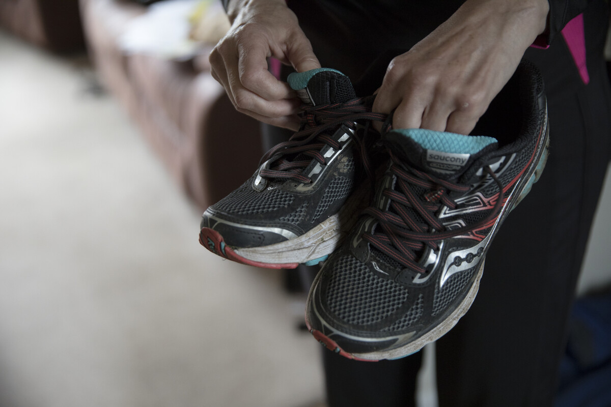 A close up of a woman's hands holding a pair of well-worn trainers