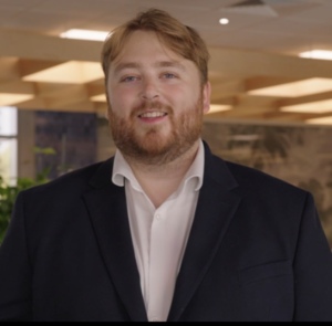 Man smiling at camera, he is wearing a white shirt and black jacket