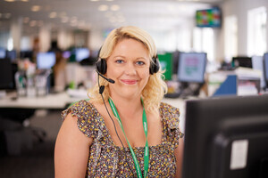 A woman sitting in front of a computer wearing a microphone headset looking at the camera.