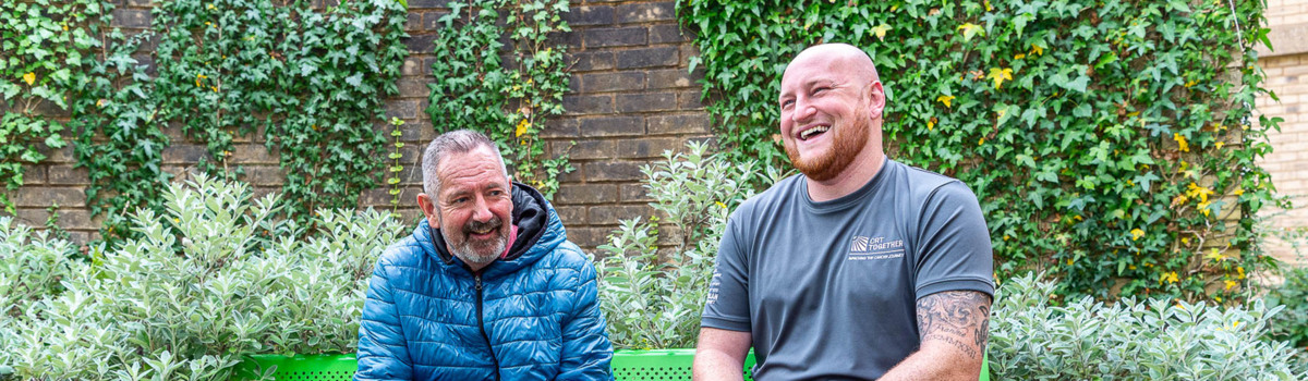A link worker and a client from CRT Together are sitting on a bench outside laughing together  