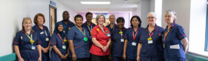 A group of healthcare professionals pose together in a hospital hallway. Most are wearing navy blue uniforms with red trim, one person wears a red uniform