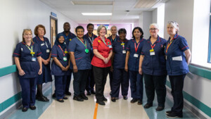 A group of healthcare professionals pose together in a hospital hallway. Most are wearing navy blue uniforms with red trim, one person wears a red uniform