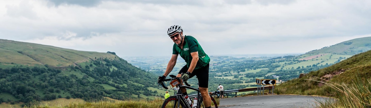 Man cycling up steep hill wearing Macmillan cycling jersey 