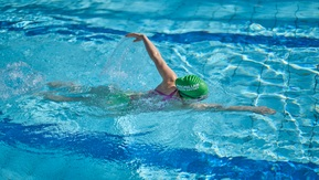 A woman in a Macmillan swimming cap does the front crawl in a swimming pool