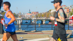 Two runners in the Amsterdam Marathon crossing over a bridge over the Amstel river. 