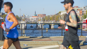 Two runners in the Amsterdam Marathon crossing over a bridge over the Amstel river. 