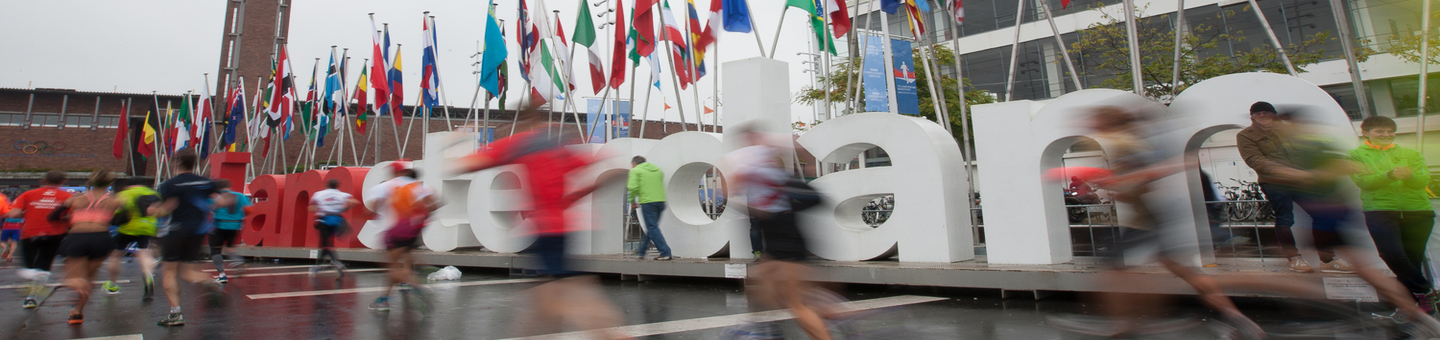Runners heading towards the Olympic stadium at the end of Amsterdam Marathon with lots of international flags next to the I am Amsterdam sign.