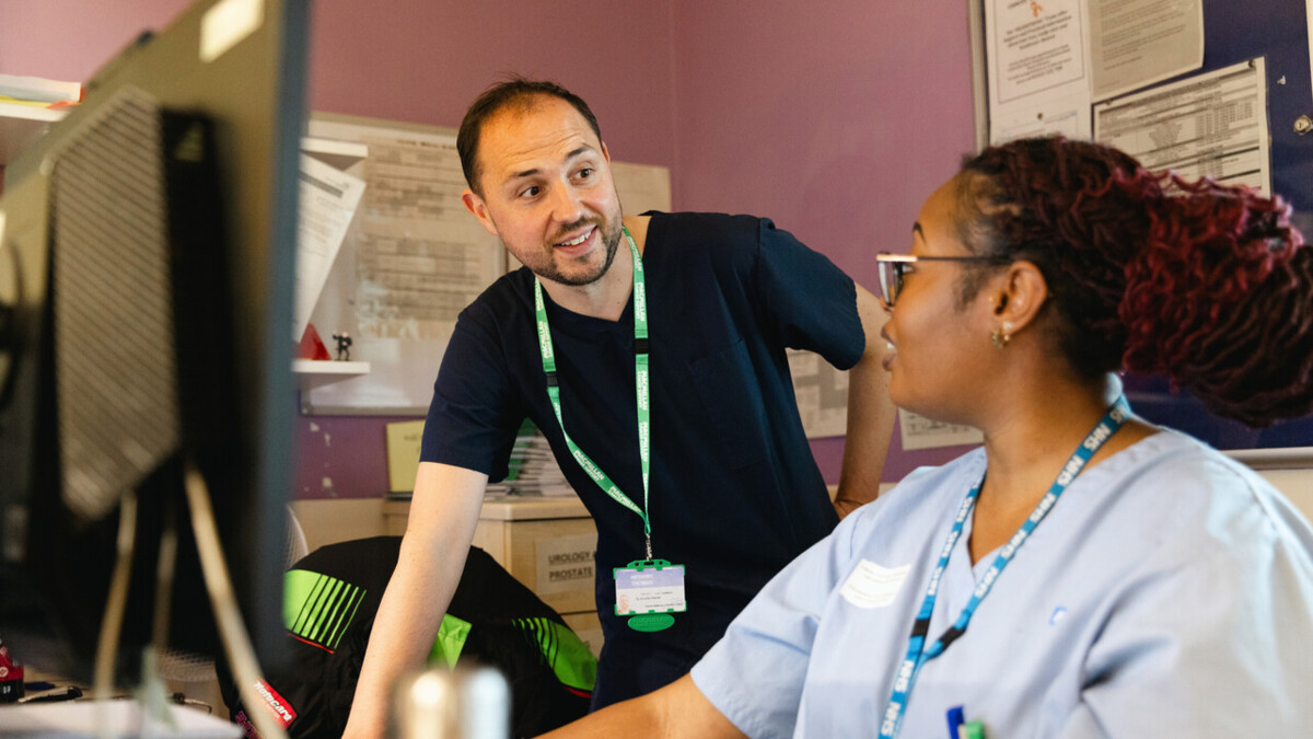 Two healthcare professionals are in front of a computer talking to each other.