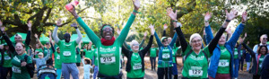 A group of event participants are standing outside with their arms in the air. Many are wearing a green Macmillan branded top. 