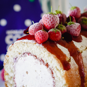 A classic arctic roll featuring a spiral of soft sponge cake wrapped around creamy vanilla ice cream, topped with glossy strawberry jam and garnished with fresh strawberries.