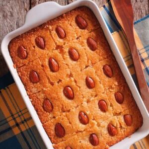 A golden tray of basbousa—soft, buttery semolina cake soaked in fragrant rose and lemon syrup—topped with whole almonds. Its rich, nutty texture and syrupy sweetness make every bite irresistible.