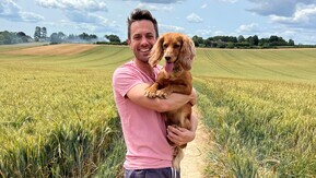 A man with brown hair wearing shorts and t-shirt holding a cute dog.
