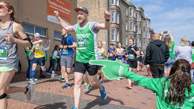 Alan running past Macmillan volunteers wearing his Macmillan running vest