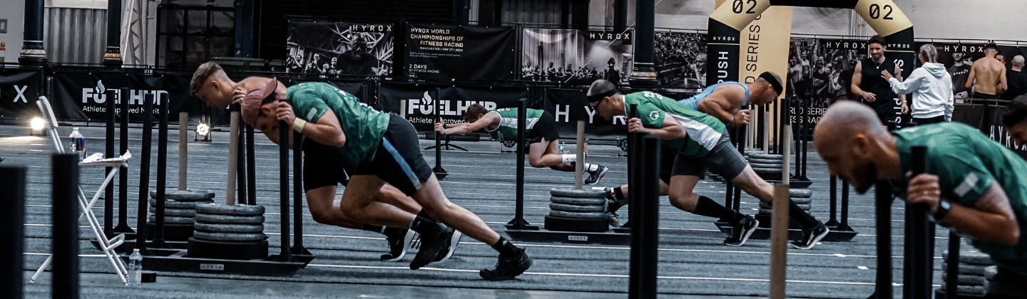 A group of people are participating in HYROX. They are pushing weight sleds across a gym floor.