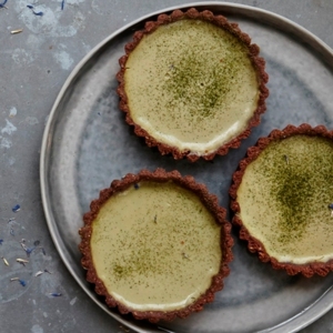 There is plate with three tarts on it. There is also a smaller plate with a tart on it that has a bite missing from it and a fork on it. The tarts have a red base. 