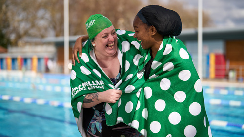 Two women in green spotty towels laughing together next to an outdoor pool