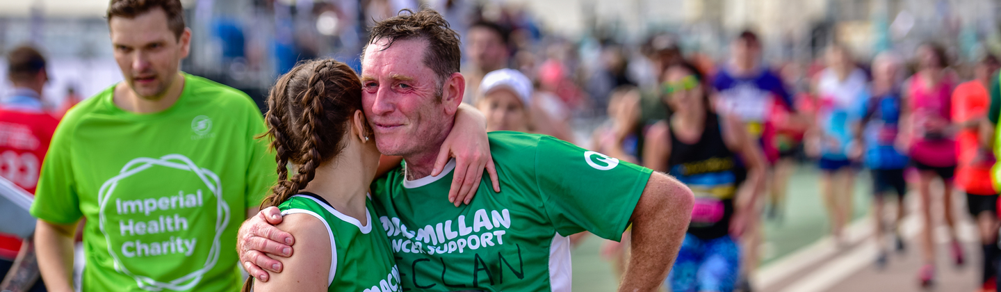 A father and daughter both wearing Macmillan running tops hugging at the end of a race