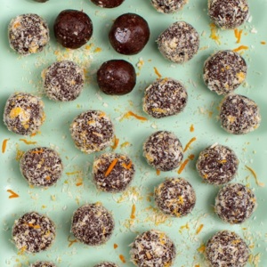 Several truffles are placed on a mint green plate. The truffles are covered in chocolate, and some have a sprinkle of desiccated coconut. Next to the plate is a bowl of desiccated coconut.