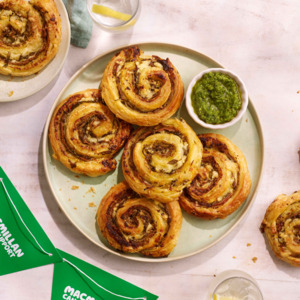 A plate of round pastry pinwheels and a small bowl of green pesto.
