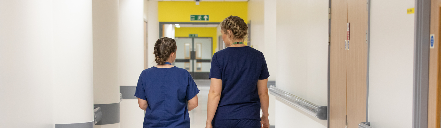 Two healthcare professionals with their back to the camera walking through a hospital hallway. 