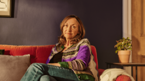A woman is sitting on her sofa at home looking at the camera.