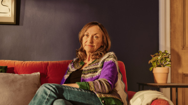 A woman is sitting on her sofa at home looking at the camera.