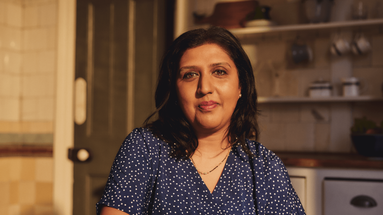 An Asian woman is sitting in a kitchen looking to camera. 