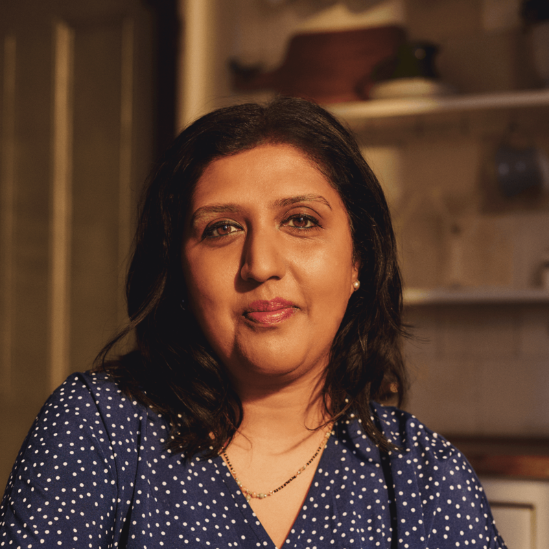 An Asian woman is sitting in a kitchen looking to camera. 