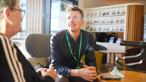 A Macmillan Support Centre staff is listening to a person talking. They are sat down in the Macmillan Horizon Centre. 