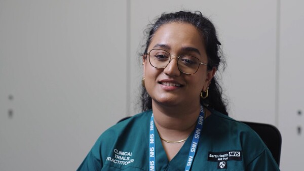 A women wearing an NHS uniform is sitting in a clinical setting and talking to the camera
