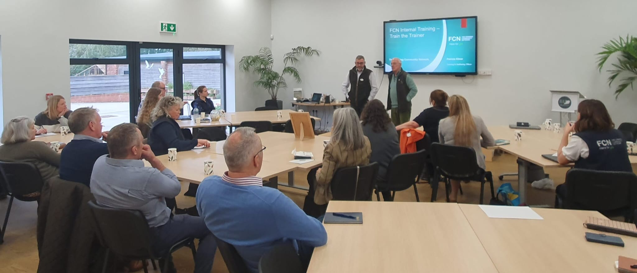 group of people listening to a speaker at a training session. They are sat around tables.