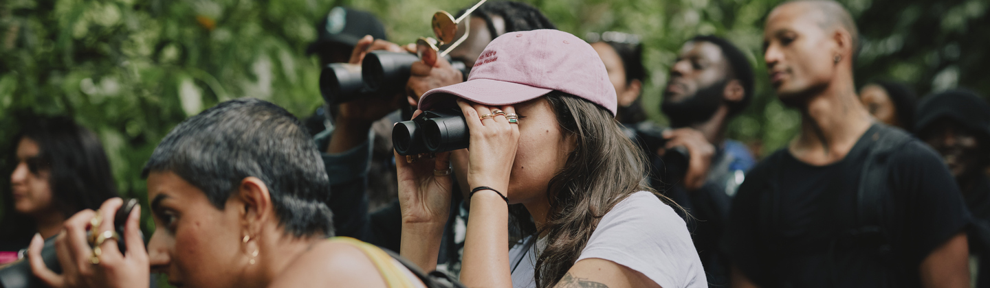 A group of people have gathered for bird watching. Many of them are holding binoculars. Photography by Rebecca Naen.