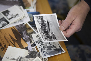 A close up of someone holding a black and white photo, with more photos sitting on the table underneath
