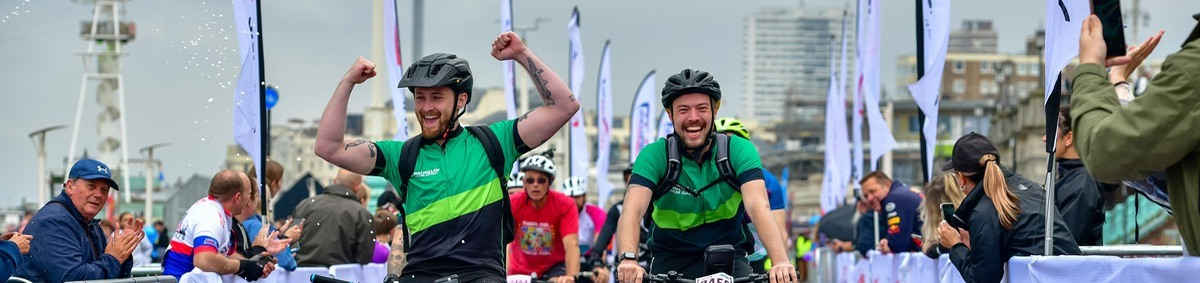 Two men on bikes wearing green Macmillan cycling tops coming over the London to Brighton finish line