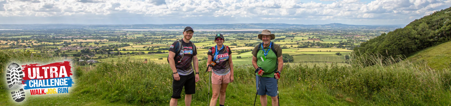 Three people are standing together in a field. Behind them is a view of the valley below.