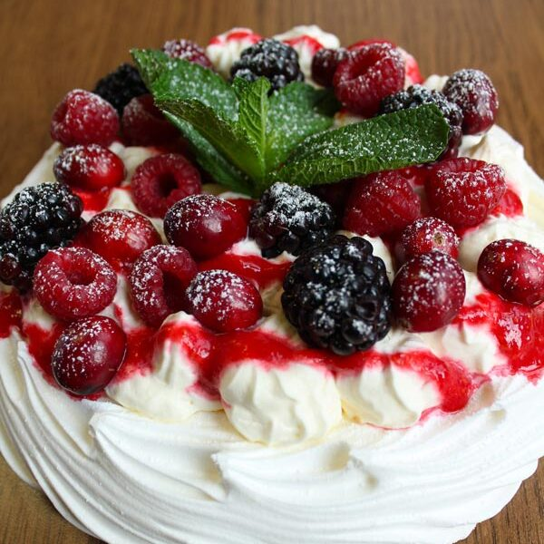A vegan pavlova topped with a bed of fresh raspberries and blackberries. These are sat on top of fresh whipped vegan cream.