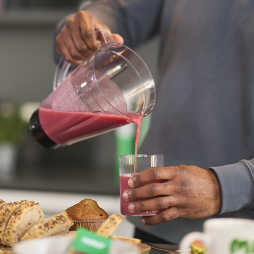 A person is pouring a pink coloured smoothie into a glass from a blender.