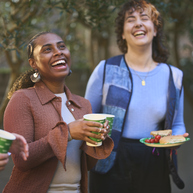 A group of people are standing together in a garden. They are laughing and enjoying themselves at a Coffee Morning. 