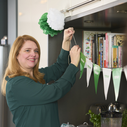 A person is putting up bunting on a bookshelf to decorate for a Coffee Morning. 