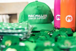 A table of Macmillan branded merchandise including caps, metal water bottles, and folded t-shirts.