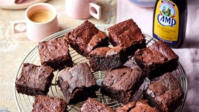 Fudgy chocolate brownies with crackled tops on a cooling rack, served with coffee, whipped cream, and Camp Coffee essence.