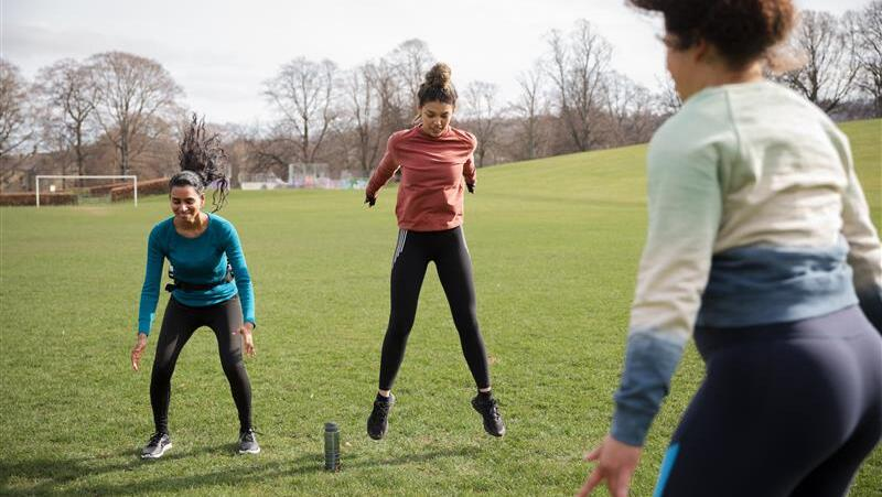 Three people are exercising on a football field pitch. They are captured mid burpee. They are wearing athletic clothing like trainers. 