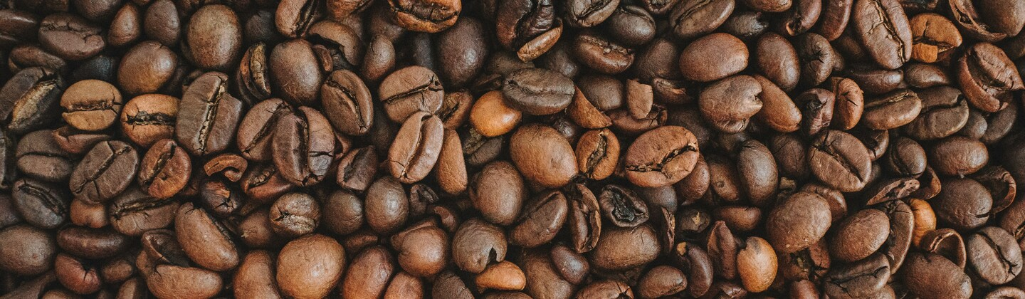 Coffee beans are spread out across the image. Photo by Anastasiia Chepinska on Unsplash.