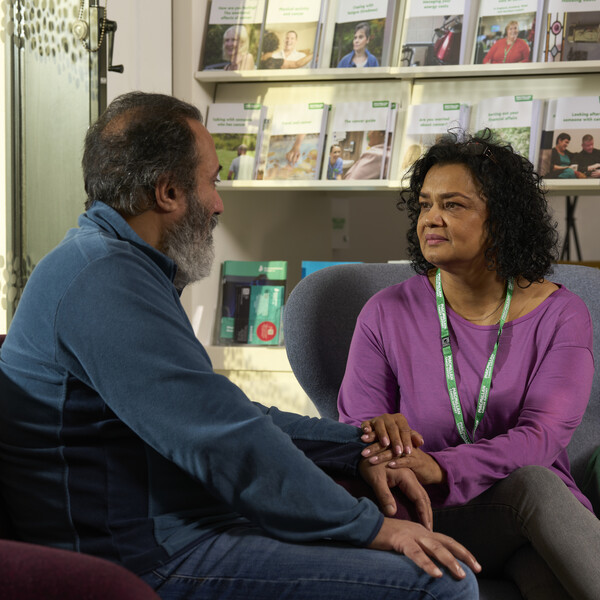 A Macmillan support worker with a patient at an information and support centre. They are holding their hand in a comforting way.