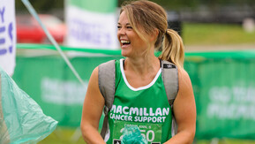 A woman at a fundraising event wearing a green, Macmillan running vest. She's looking away from the camera and smiling.
