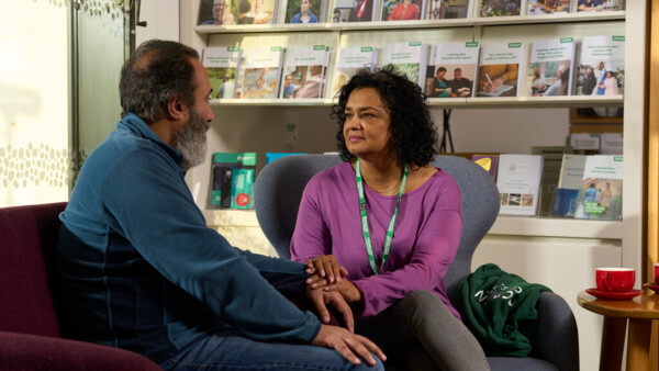 A Macmillan support worker with a patient at an information and support centre. They are holding their hand in a comforting way.