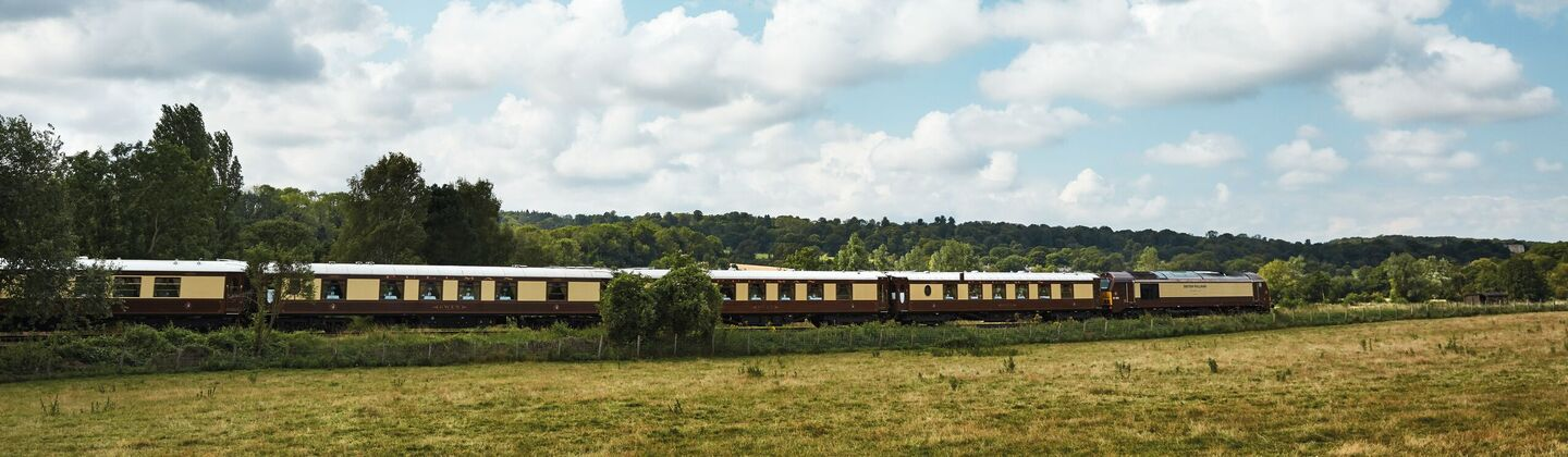A train is travelling on tracks next to a grass field on a partly cloudy day.
