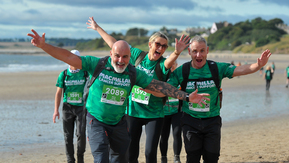 People walking along a beach waving at the camera