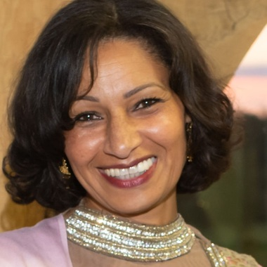 Woman with dark hair smiling at camera she is wearing a pink dress with silver and gold detailing 