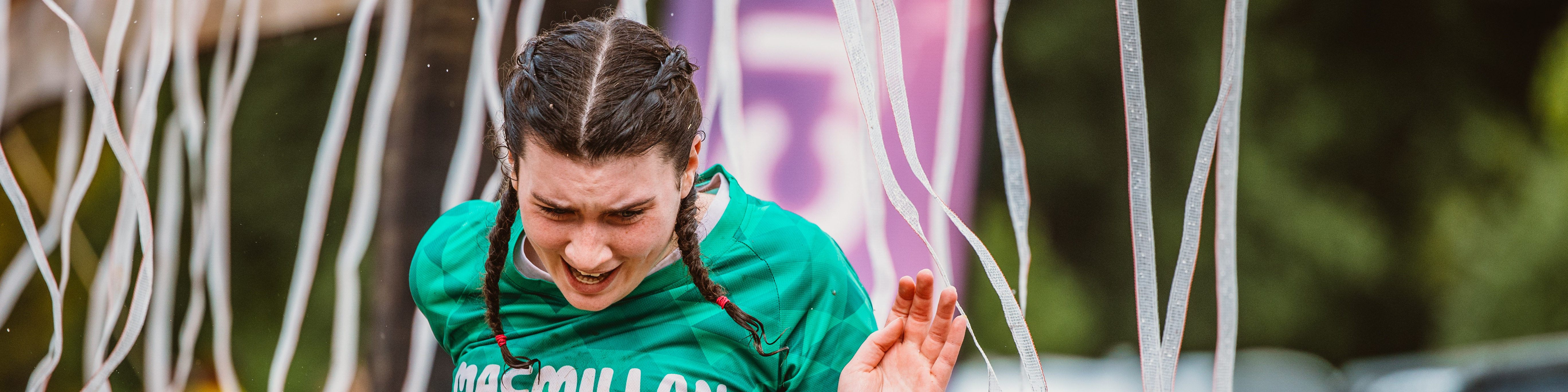 A woman with pigtails wearing a Macmillan t-shirt and running through electric shock curtain 
